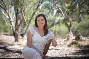 woman in white dress sitting on chair smiling amongst australian bush